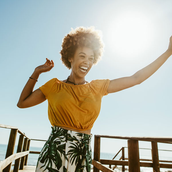 A woman in a yellow shirt and green skirt arms outstretched after dental treatment in Flagstaff, AZ
