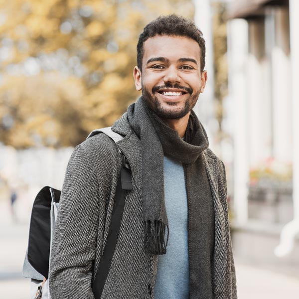 A young man with a backpack and scarf smiles in Flagstaff, AZ