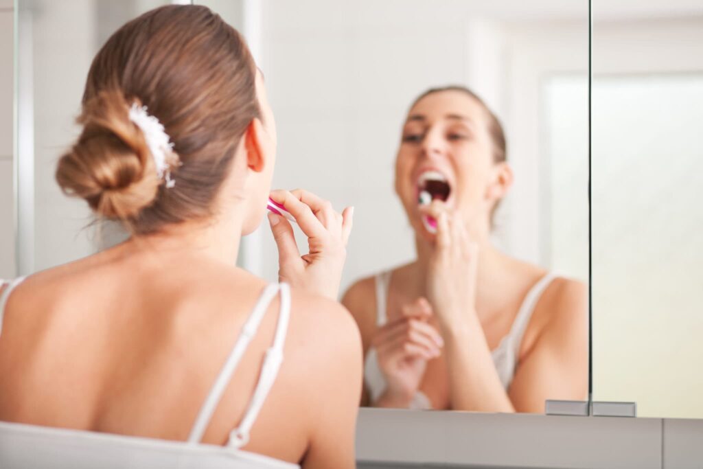 Young woman with light brown hair brushing her teeth after happily waking up in the morning